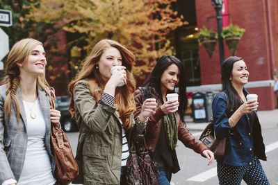 Happy female friends having coffee while walking on city street