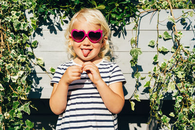 A funny little girl in sunglasses shows her tongue.