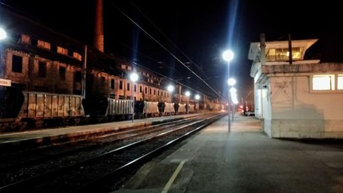 Illuminated railroad station by buildings in city at night