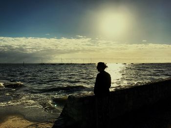 Silhouette man sitting on beach against sky during sunset
