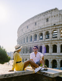 Woman sitting on historical building against sky