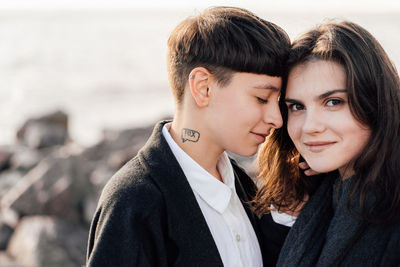 Lesbian women embracing while standing on rock against sea