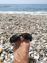 Low section of man standing on pebbles at beach