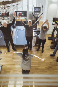 High angle view of female caregiver assisting senior men and women to exercise at nursing home