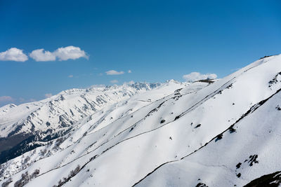 Scenic view of snow covered mountains against blue sky