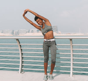 Portrait of smiling woman stretching hands on bridge over sea