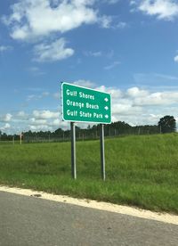 Road sign on field against sky