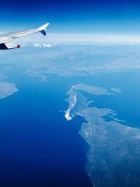 Aerial view of airplane flying over sea against blue sky