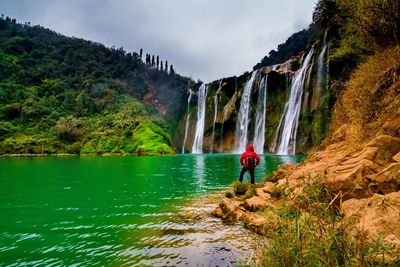 Man standing on cliff by river against sky