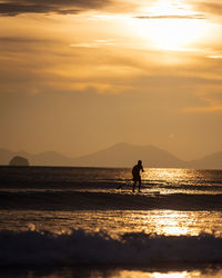 Silhouette man in sea against sky during sunset