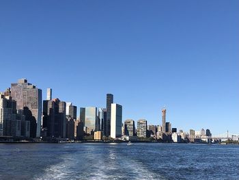 Sea by modern buildings against clear blue sky