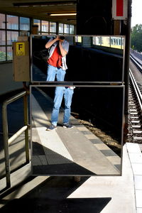 Rear view of man standing by railing on sunny day
