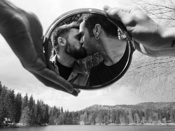 Men kissing on mouth reflecting in mirror held by hands