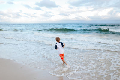 Full length of boy running on beach against sky