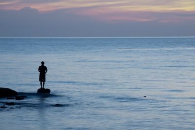 Silhouette man standing in sea against sky during sunset