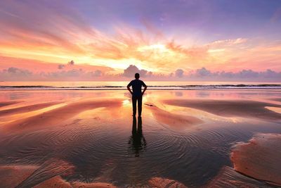Rear view of man standing on beach during sunset