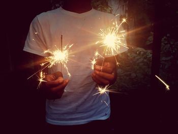 Midsection of man holding sparklers while standing in yard