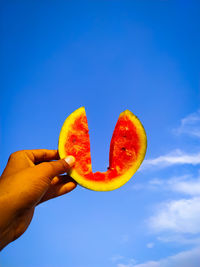 Low angle view of hand holding fruit against blue sky