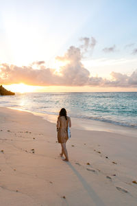 Rear view of woman on beach against sky during sunset