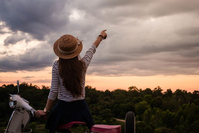 Rear view of woman gesturing towards cloudy sky