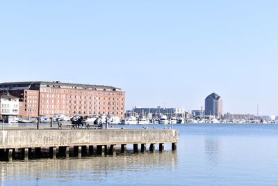 Buildings by river against clear blue sky