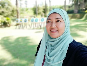 Close-up of smiling woman in hijab looking away while standing in park