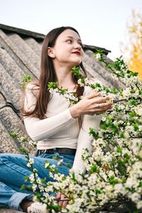 Smiling woman sitting on roof by white flowering plant