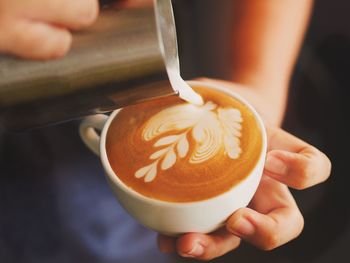 Cropped image of person making froth art on coffee