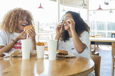 Positive african american female friends sitting at table with fast food and drinks and enjoying weekend in cafe