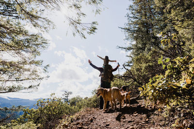 Male hiker carrying daughter while standing by dogs on mountain against sky