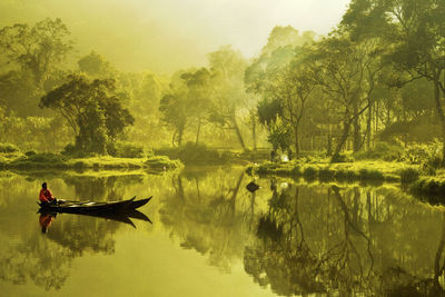 Man sitting on boat in lake against trees