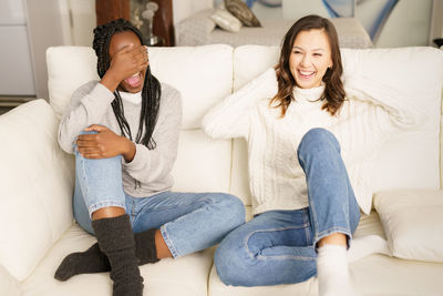 Full length of smiling friends sitting on sofa at home