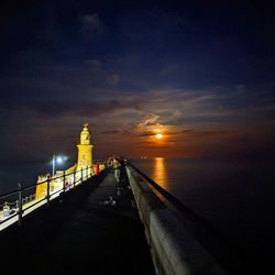 Illuminated building by sea against sky at night