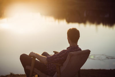 Man relaxing in the seat at bank of lake watching sunset