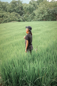 Side view of woman holding flower standing on grass against tree