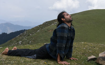 A long haired handsome young indian man doing ashtanga, bhujangasana cobra yoga pose in the mountain 