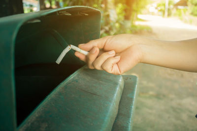 Cropped hand of woman throwing cigarette in garbage can