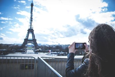 Man photographing with mobile phone against sky