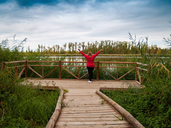 Rear view of woman standing on footbridge against lake