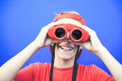 Portrait of smiling boy looking through binoculars against blue background