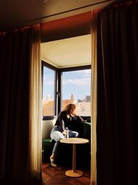 Woman looking through window while sitting on chair