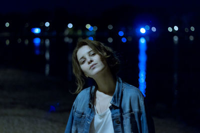 Portrait of young woman standing against illuminated lights at night