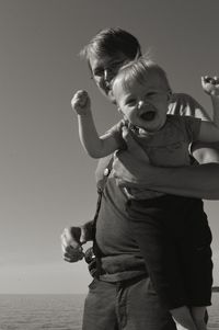 Low angle view of father carrying son while standing at beach