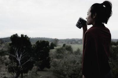 Side view of young woman standing against sky