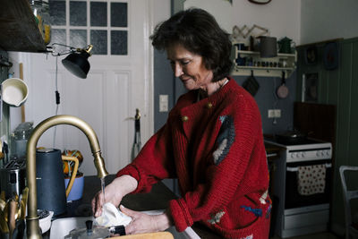 Senior woman washing mug in kitchen sink at home