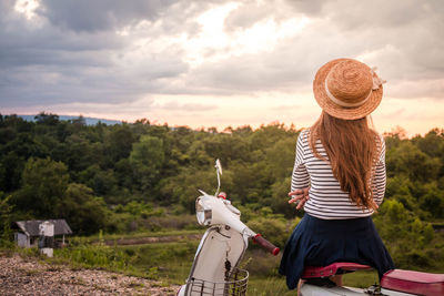 Rear view of woman sitting on motor scooter against cloudy sky