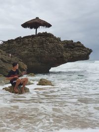 Man sitting on rock by sea against sky