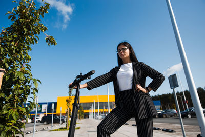 Low angle view of woman with push scooter standing against blue sky