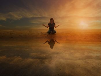 Full length of woman meditating at beach sky during sunset