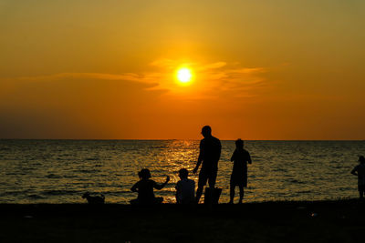 Silhouette people on beach against sky during sunset